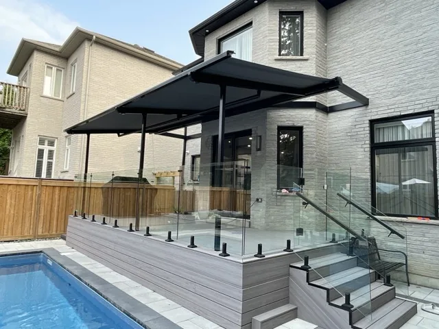 Black retractable awning extended over elevated pool deck with glass railing