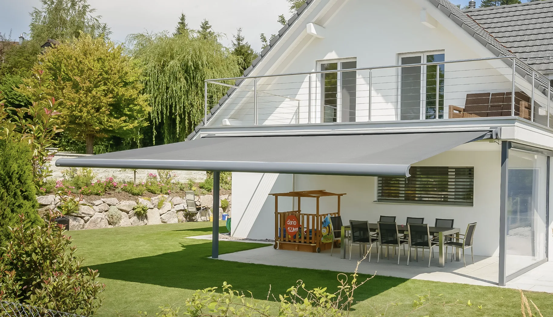 Grey retractable awning extended over patio dining set beside house