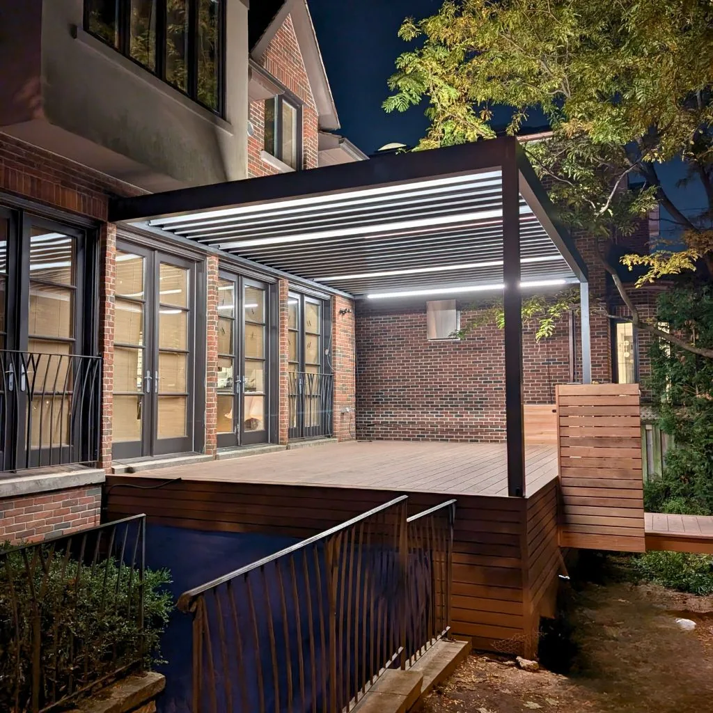 Louvered pergola with built-in LED lighting over backyard deck at night