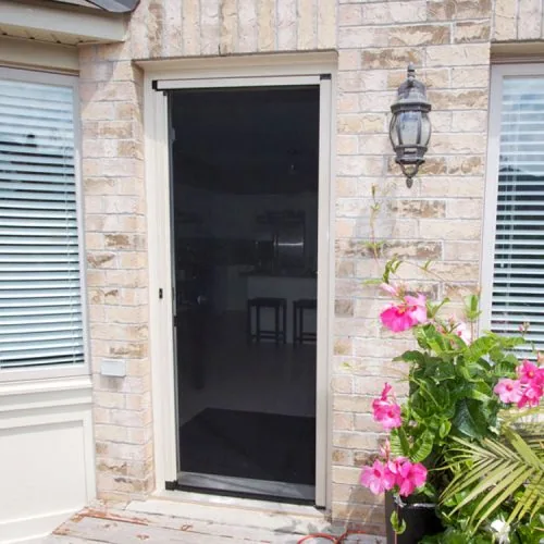 Dark vertical bug door screen covering entry door beside brick exterior and flowers