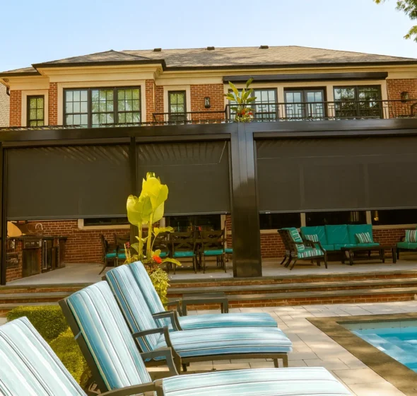 Louvered aluminum pergola on a large brick home, enclosed with dark motorized retractable screens over a poolside patio