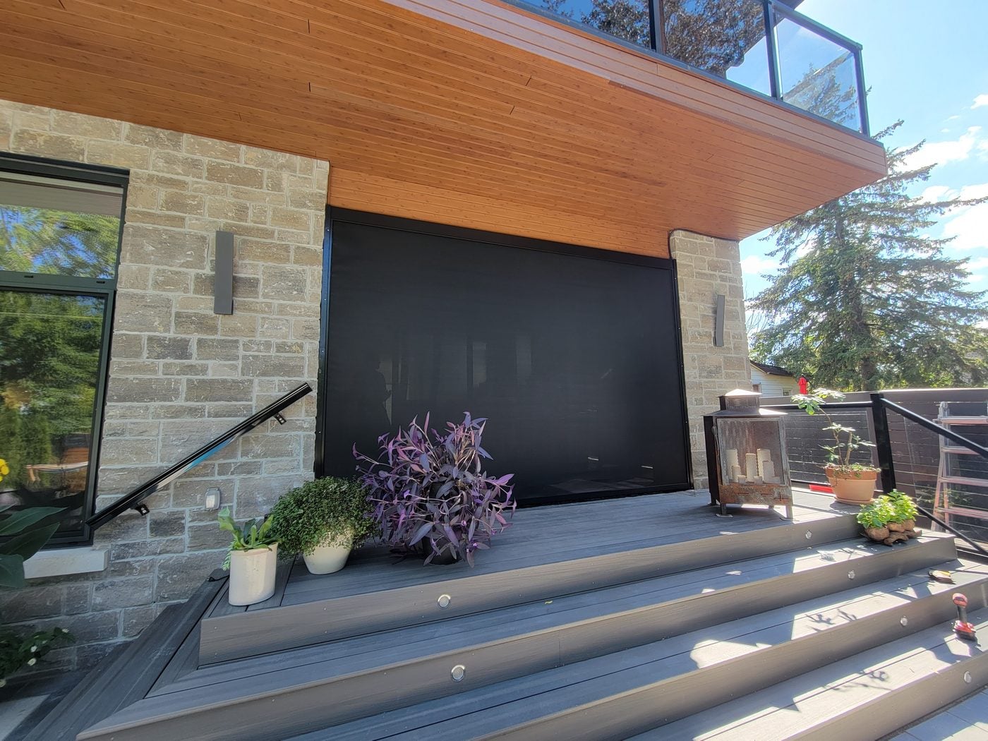 Large black retractable screen fully lowered on a stone and wood porch