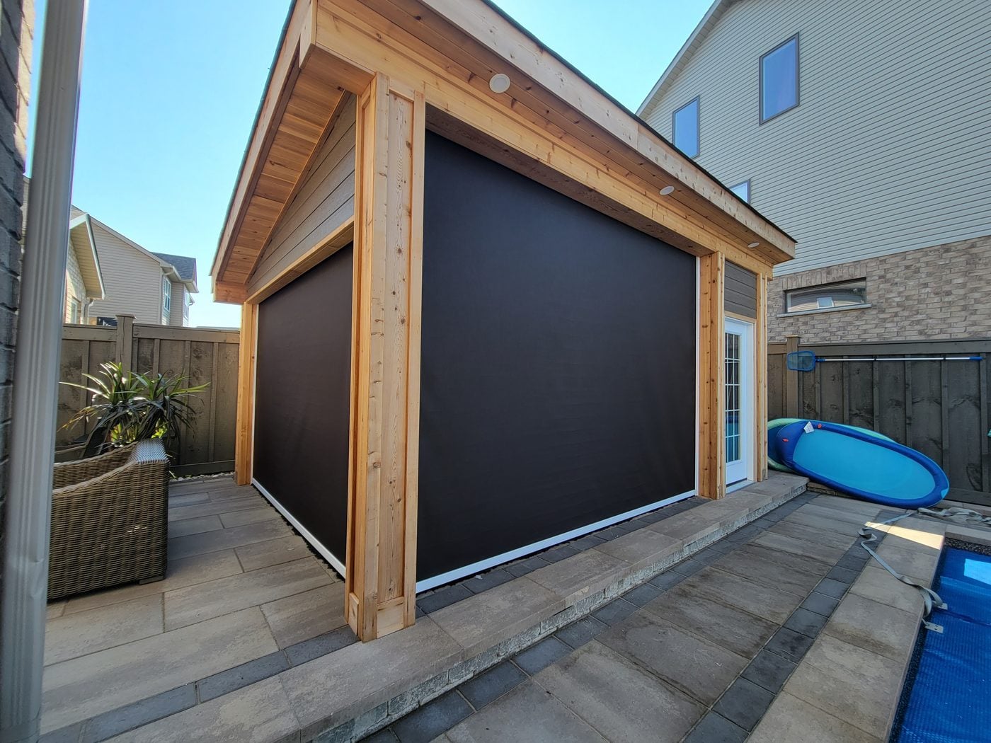 Pergola-style patio by a pool with black retractable screens lowered on two sides