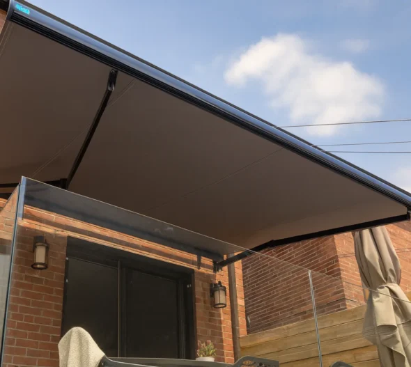 Wall-mounted retractable awning fully extended over a brick-house patio with a glass balustrade