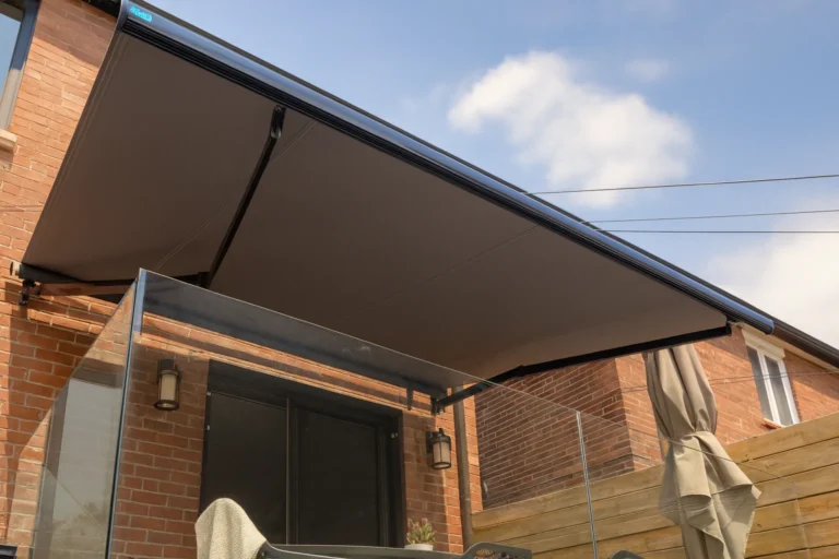 Wall-mounted retractable awning fully extended over a brick-house patio with a glass balustrade