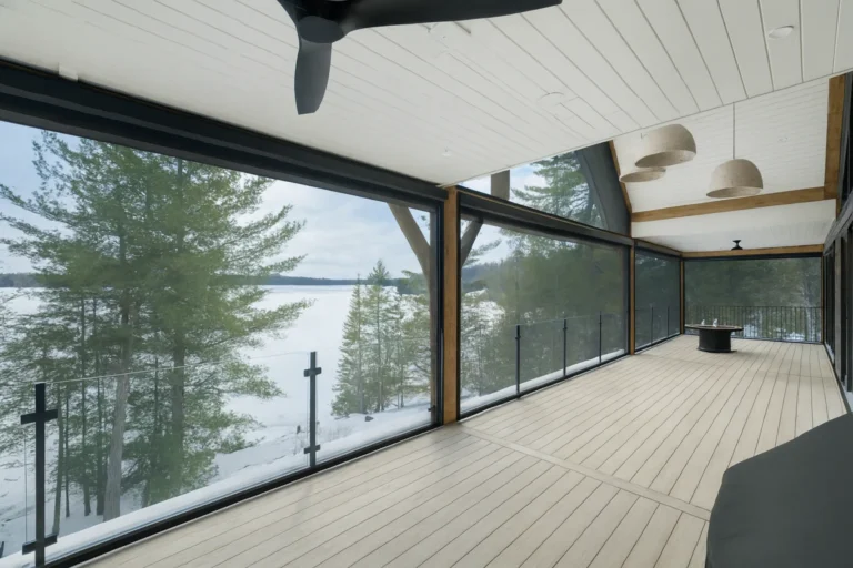 Dark motorized retractable screens lowered around a covered lakeside deck at dusk, warm lighting under a wood ceiling